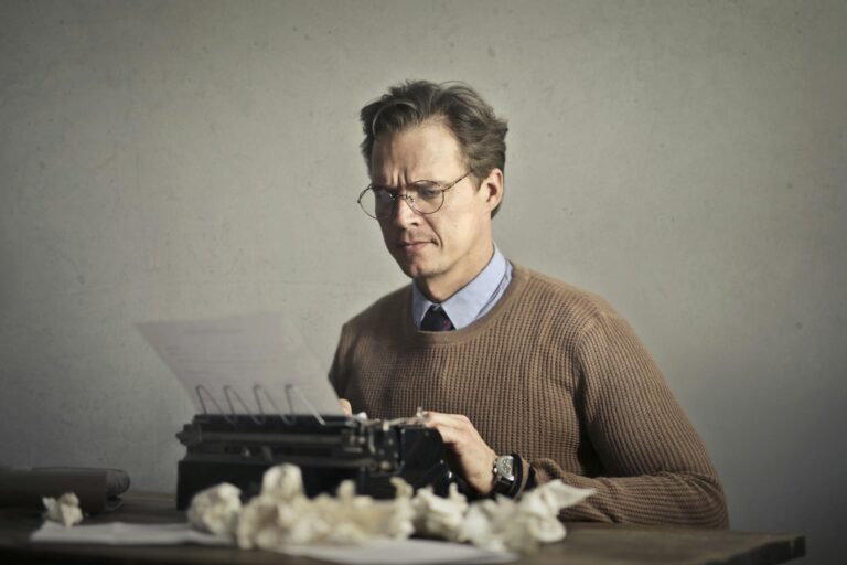 Adult frowned male writer working on typewriter at home