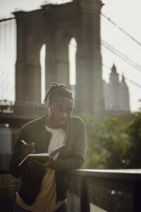 Positive black male freelancer writing ideas while standing on city embankment